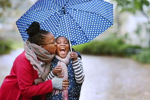 Mom kissing her daughter under an umbrella.